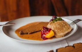 Hirschbraten mit dickem Wurzelsaft und Knödel, © Niederösterreich Werbung/Daniela Führer Ein Teller mit Hirschbraten, Knödeln, Preiselbeeren und Gemüse.