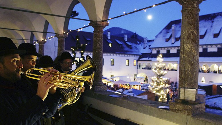 Flammende Weihnacht, © weinfranz.at Musiker spielen Trompeten auf einem Balkon mit Blick auf einen Weihnachtsmarkt bei Nacht.