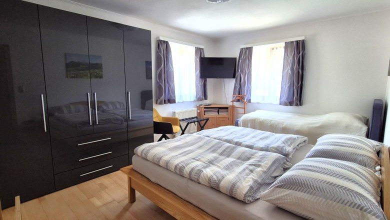 Ferienwohnung Schindlegger, © Familie Schindlegger Schlafzimmer mit zwei Betten, einem großen schwarzen Kleiderschrank, einem Fernseher und zwei Fenstern mit Vorhängen.