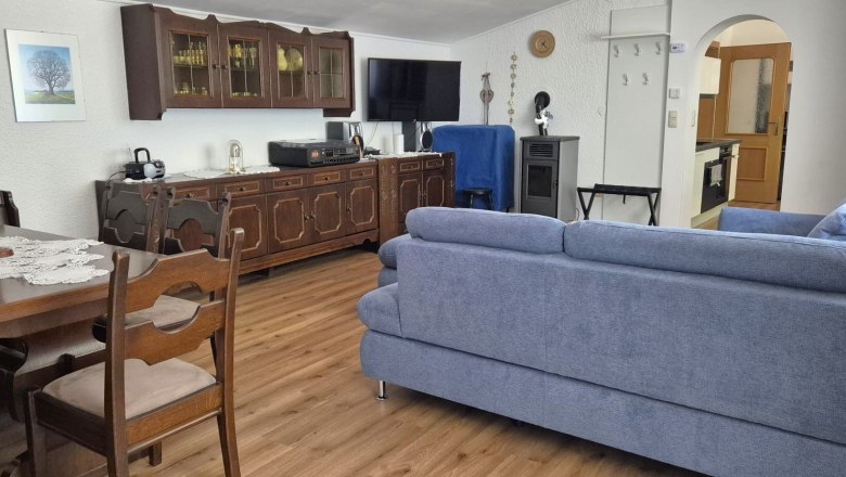 Ferienwohnung Schindlegger, © Familie Schindlegger Wohnzimmer einer Ferienwohnung mit blauer Couch, Holzmöbeln und Esstisch.