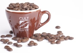 Cult Caffè, © zVg Cult Caffè Braune Tasse mit Aufschrift 'Cult Caffè', gefüllt mit Kaffeebohnen, auf weißem Hintergrund.