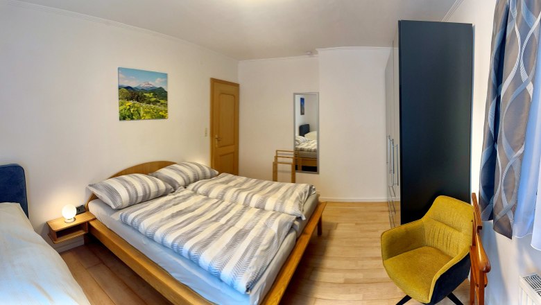 Ferienwohnung Schindlegger, © Familie Schindlegger Ein Schlafzimmer mit einem Doppelbett, einem gelben Stuhl, einem Schrank.