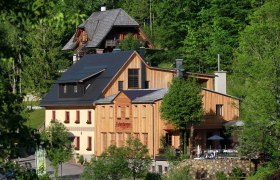 Fahrnberger, © Dagmar Nahringbauer Ein traditionelles Gebäude mit Holzfassade in einer grünen Waldlandschaft.
