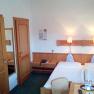 Doppelzimmer, © Hotel Zum Goldenen Hirschen Ein Hotelzimmer mit zwei Einzelbetten, Holzmöbeln und grüner Teppichboden.