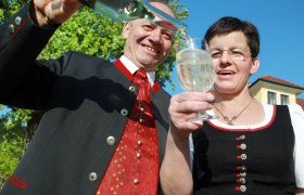 Mostbaron Wieser, © Mostviertel Tourismus, weinfranz.at Zwei Personen in traditioneller Kleidung stoßen mit einem Glas an, während eine Flasche eingeschenkt wird.