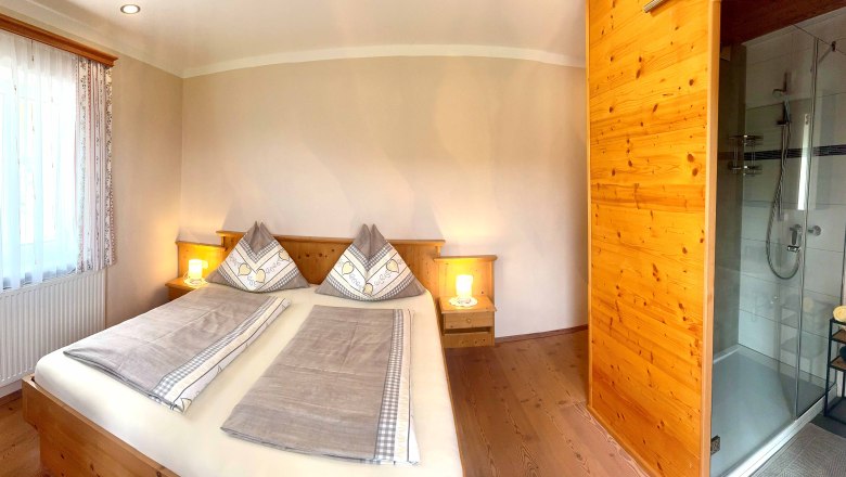 Urlaub am Moaserhof, © Familie Buber Gemütliches Schlafzimmer mit Doppelbett, Holzmöbeln und angrenzendem Badezimmer mit Dusche.