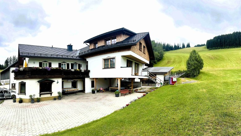 Urlaub am Moaserhof, © Familie Buber Ein traditionelles Bauernhaus mit Holzverkleidung und Blumen auf dem Balkon, umgeben von grünen Wiesen und Wäldern.