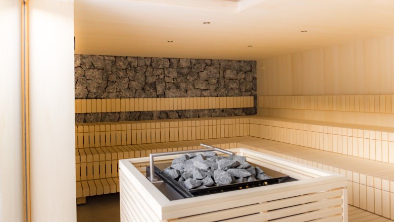 Ybbstaler Solebad, © Rene Jagersberger Innenansicht einer modernen Sauna mit Holzbänken und einem Ofen mit Steinen in der Mitte.