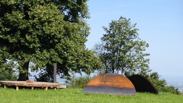 Rund um Schau, © Mostviertel Tourismus Holzplattform und Metallskulpturen auf einer Wiese mit Bäumen im Hintergrund.