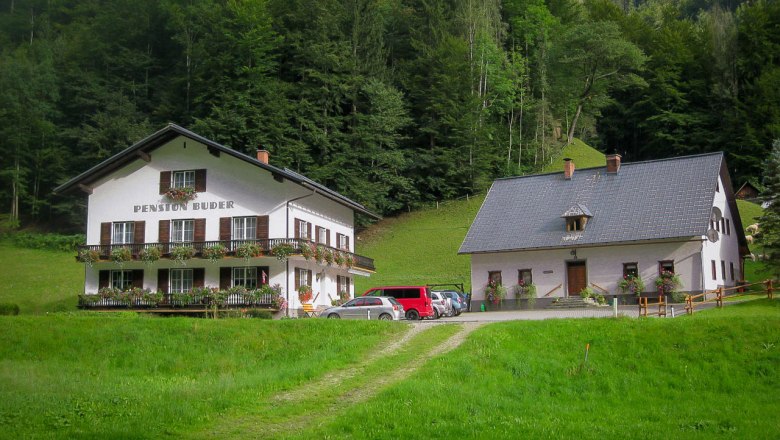 Mendlingbauer, © Mendlingbauer Zwei traditionelle Gebäude in einer grünen, bewaldeten Umgebung.