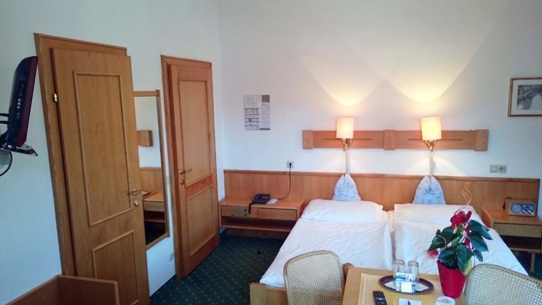 Doppelzimmer, © Hotel Zum Goldenen Hirschen Ein Hotelzimmer mit zwei Einzelbetten, Holzmöbeln und grüner Teppichboden.