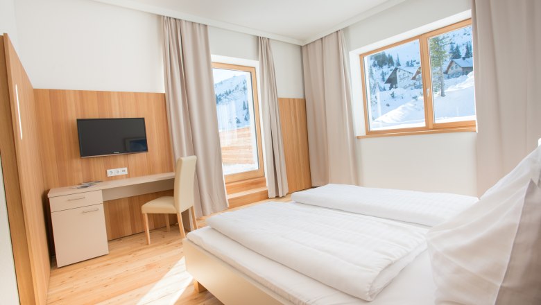 JoSchi Sporthaus Hochkar, © JoSchi Sporthaus Hochkar Helles Hotelzimmer mit Doppelbett, Schreibtisch und Blick auf verschneite Berge.