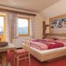 Erlebniszimmer Auf der Alm, © Fam. Helmel Gemütliches Zimmer im Alpenstil mit Holzmöbeln, rotem Teppich und Bergblick.