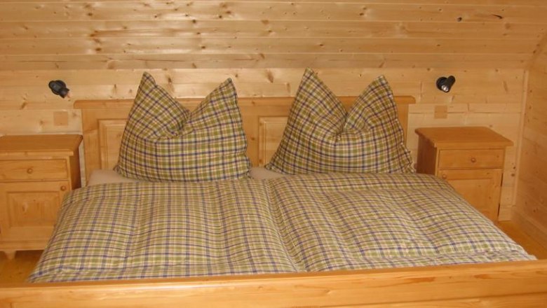Feriendorf Lassing-Hochkar, © Feriendorf Lassing Holzschlafzimmer mit kariertem Doppelbett und Nachttischen.