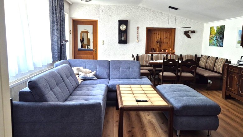Ferienwohnung Schindlegger, © Familie Schindlegger Gemütliches Wohnzimmer mit blauer Couch, Holztisch und Essbereich in einer Ferienwohnung.