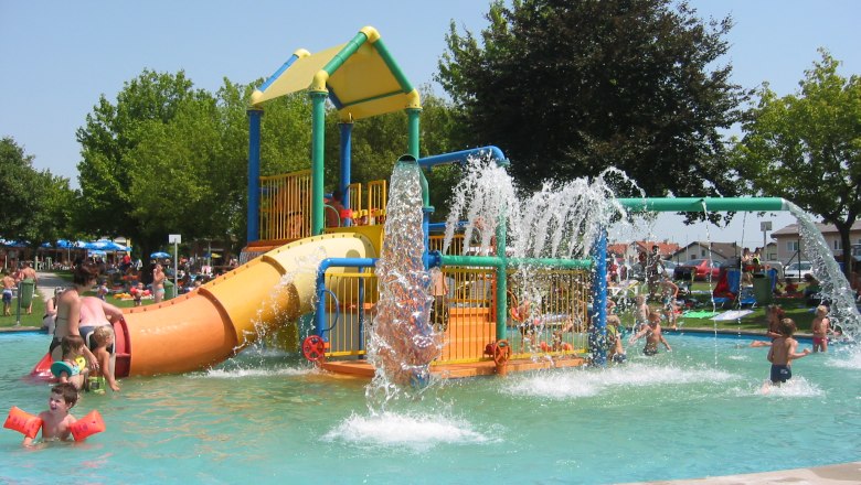 Kinder spielen in einem Wasserspielgarten mit Rutschen und Wasserfont&auml;nen.