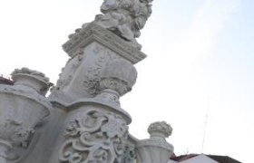 Nahaufnahme einer kunstvoll verzierten S&auml;ule mit Skulpturen und Ornamenten, im Hintergrund Geb&auml;ude und blauer Himmel.