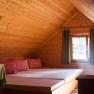 Gemütliches Dachzimmer mit Holzverkleidung, Betten und karierten Kissen.