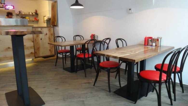 Innenansicht eines modernen Restaurants mit Holztischen und roten Stühlen.