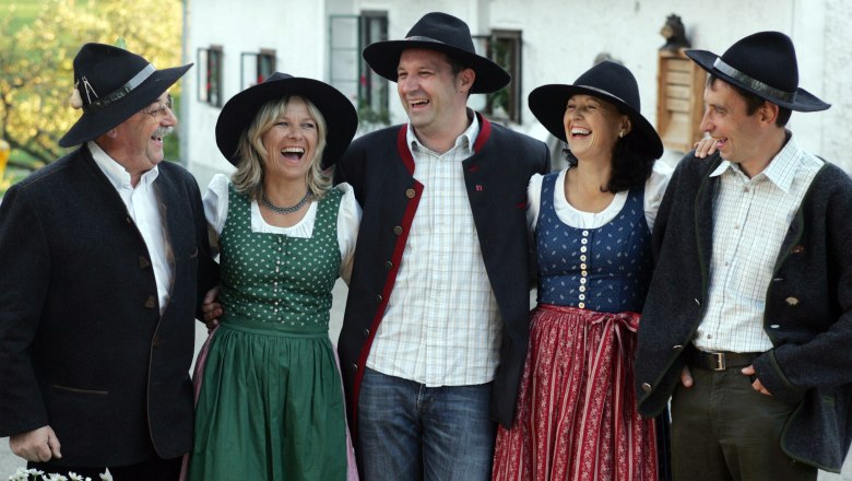 Gruppe von fünf Personen in traditioneller bayerischer Tracht, die fröhlich lachen.