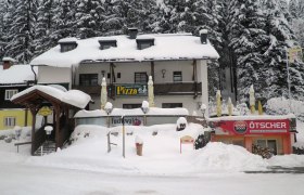 Verschneites Pizza-Restaurant Fuchswald mit umliegenden Bäumen.