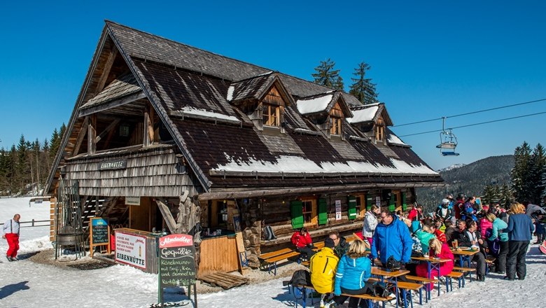 Eine Berghütte im Schnee mit Menschen, die draußen sitzen.
