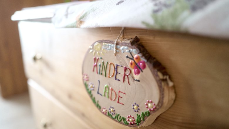 Nahaufnahme eines Holzschildes mit der Aufschrift 'Kinderlade' an einer Kommode.