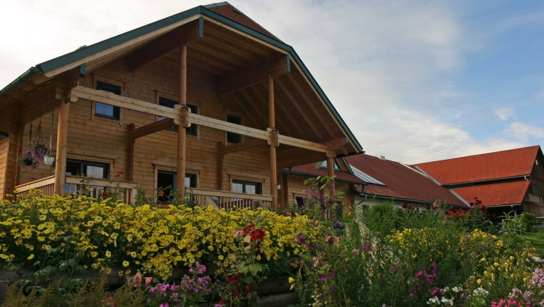 Ferienwohnung Herdengl Bauernhaus, © Tourismusverein Ein traditionelles Bauernhaus mit Holzverkleidung und einem blühenden Garten im Vordergrund.