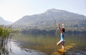 Eine Frau macht Yoga in einem See mit einem Berg im Hintergrund.