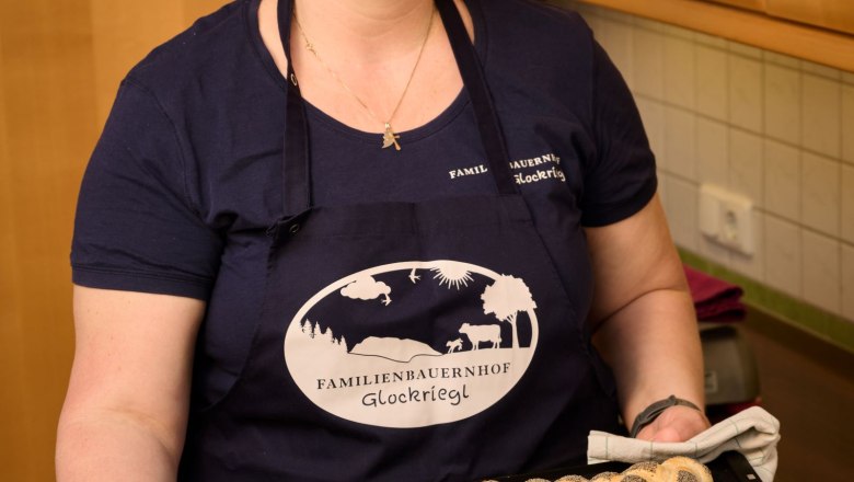Eine Frau in einer K&uuml;che h&auml;lt ein Blech mit frisch gebackenen Mohnbr&ouml;tchen.