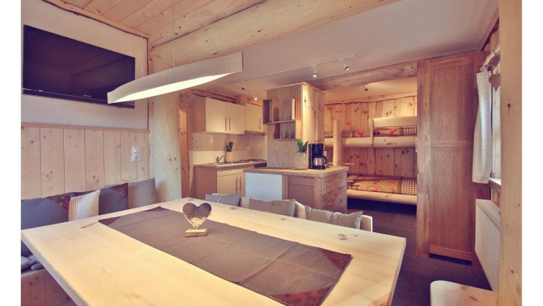 Innenansicht eines gemütlichen Chalets mit Holzmöbeln, Esstisch, Küche und Etagenbetten.