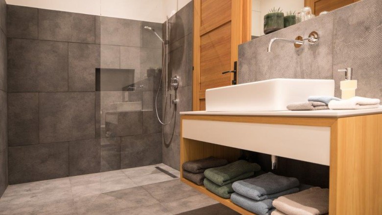 Modernes Badezimmer mit grauen Fliesen, einer Glasdusche und einem Holzwaschtisch mit Handt&uuml;chern.