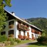 Ein traditionelles Haus mit Blumenk&auml;sten vor einem bewaldeten Berg.