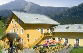 Gelbes Gebäude mit Terrasse und bunten Sonnenschirmen, umgeben von Bergen.