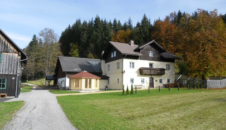Ein großes, zweistöckiges Haus mit Balkon, umgeben von Wiesen und Bäumen im Herbst.
