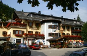 Ein traditionelles Gasthaus mit blumengeschmückten Balkonen und geparkten Autos davor.