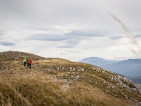 Die Wanderer genie&szlig;en die frische Bergluft und die atemberaubende Aussicht auf die sanften H&uuml;gel und schroffen Gipfel. Umgeben von einer malerischen Landschaft, in der das goldene Gras sanft im Wind wiegt, l&auml;dt die Natur zu unvergesslichen Erlebnissen ein.