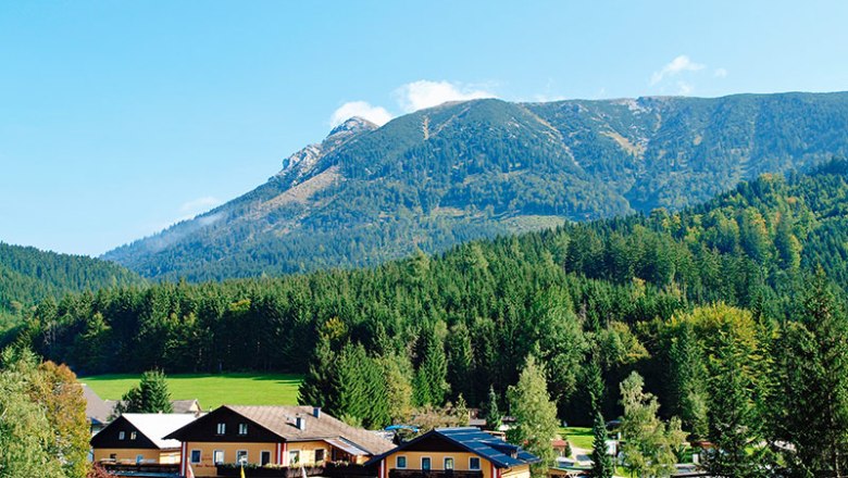 Blick auf ein Campinggelände mit Gebäuden vor einem bewaldeten Bergmassiv.