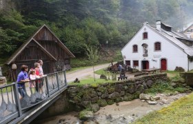 Eine Familie steht auf einer Br&uuml;cke vor einem historischen Geb&auml;ude in einer l&auml;ndlichen Umgebung.
