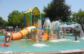 Kinder spielen in einem Wasserspielgarten mit Rutschen und Wasserfont&auml;nen.