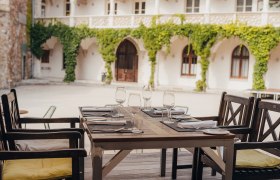Ein gedeckter Tisch in einem historischen Innenhof mit Weinreben an den Wänden.