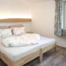 Gem&uuml;tliches Schlafzimmer mit Doppelbett, Holzboden und Fenster mit Vorh&auml;ngen.