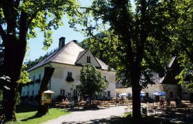 Ein Herrenhaus mit Biergarten im Gr&uuml;nen, umgeben von B&auml;umen.