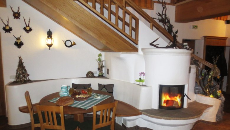 Gemütlicher Innenraum mit Kamin, Holztisch und Treppe.