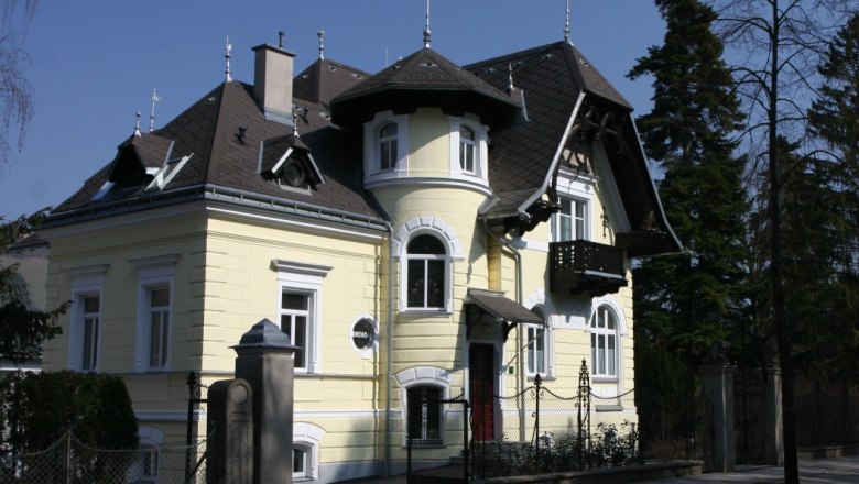 Au&szlig;enansicht einer gelben Villa mit T&uuml;rmchen und Balkon.