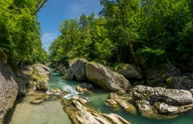 Fluss in einer bewaldeten Schlucht mit gro&szlig;en Felsen und klarem Wasser.