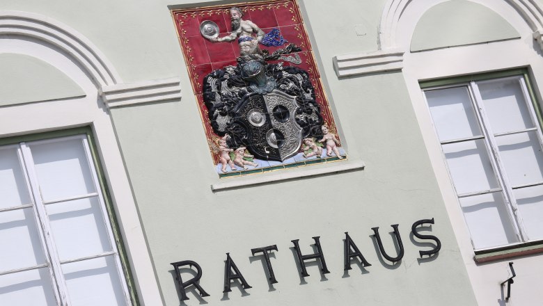 Fassade eines Rathauses mit dekorativem Wappen und Schriftzug 'Rathaus'.
