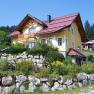 Gelbes Haus mit rotem Dach in einer grünen Landschaft.