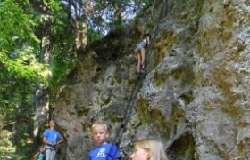 Kinder klettern an einer Felswand im Wald.