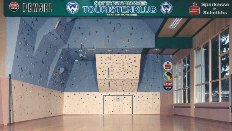 Innenansicht einer Kletterhalle mit blauer Kletterwand und bunten Griffen.
